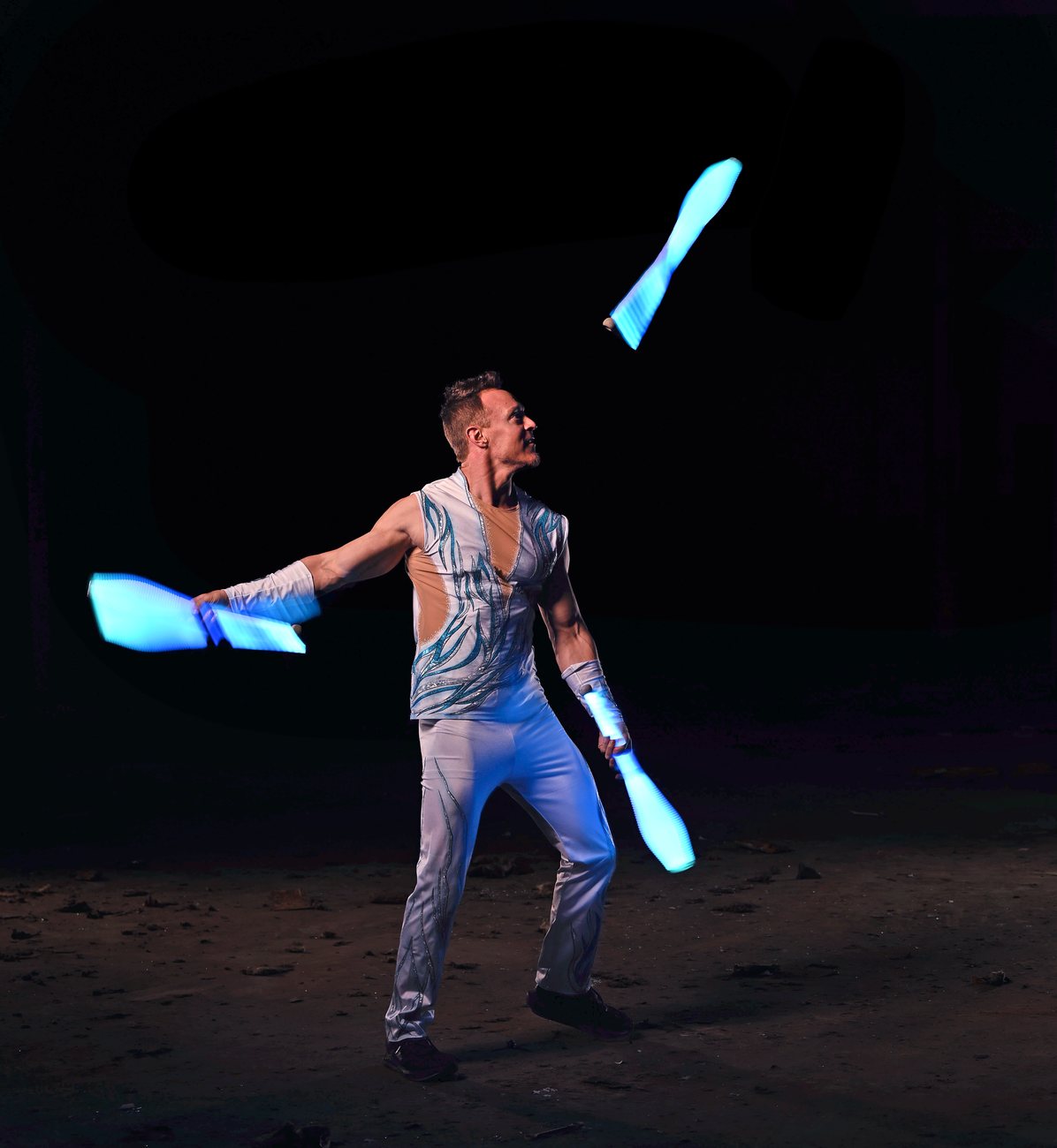 Rocco juggling glowing blue LED clubs in the dark