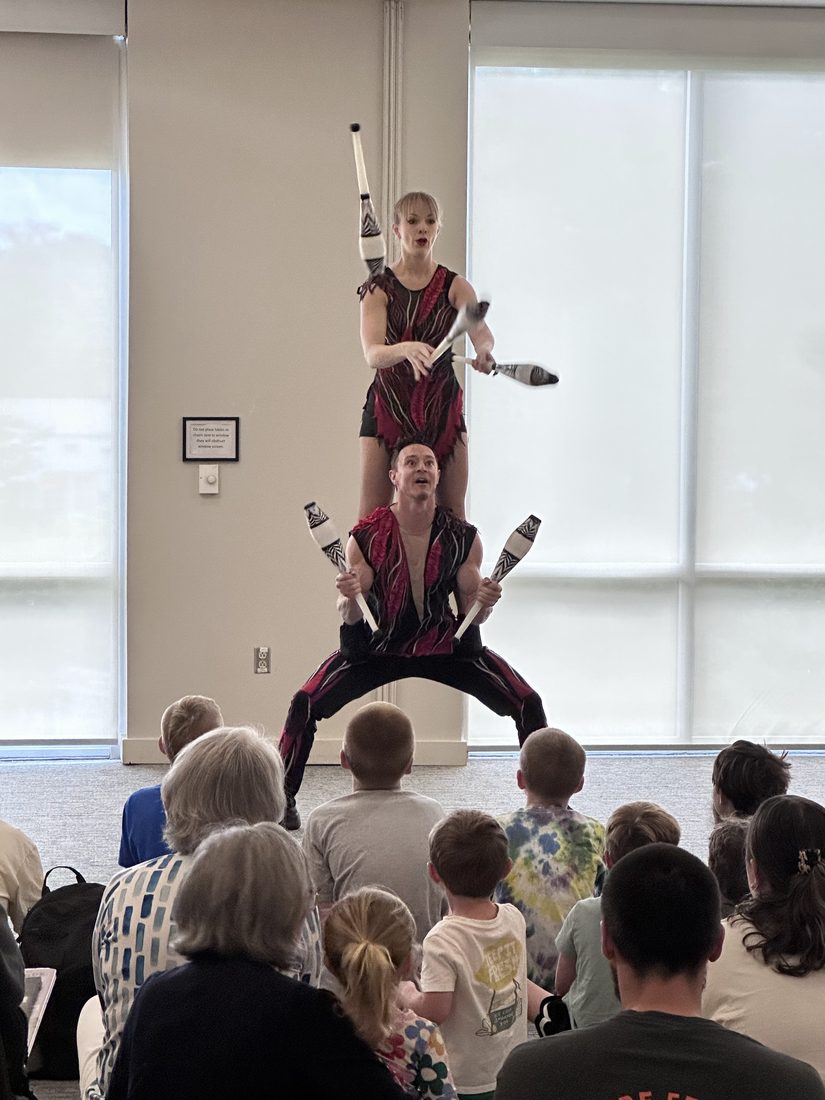 Nova balancing on Rocco's shoulders, juggling clubs in front of a packed library audience